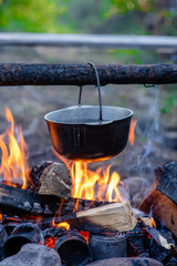 Cooking camping outdoor meal in an open fire in a travel pot with blaze