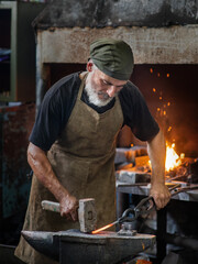 Old blacksmith working metal with hammer on the anvil in the forge