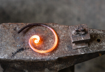 Metal object of spiral shape on an anvil in a smithy.