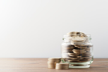 Saving money in jar. Jar filled with coins on wood table. Copy space.