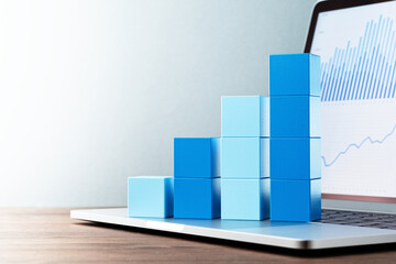Laptop and bar graph. Blue graphs on laptop screen. Stacked blue cube and laptop on wood table