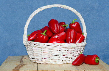 Large white basket with ripe red paprika on a wooden table. Harvest paprika, bell peppers in a basket.