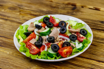 Tasty tuna salad with lettuce, black olives and fresh vegetables on wooden table