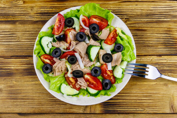 Tasty tuna salad with lettuce, black olives and fresh vegetables on wooden table. Top view