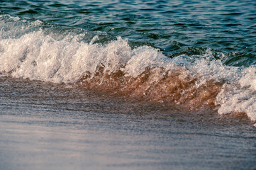 Small waves rolling onto a sandy beach pulling sand back up the face of the wave