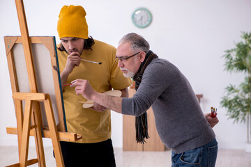 Old man taking lesson from young painter