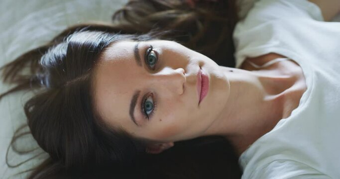 Authentic close up shot of healthy happy woman is smiling in camera just woke up with a sun beams in her bedroom in a morning. Concept: wellbeing, healthcare, lifestyle, bedding, happiness, femininity