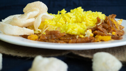Nasi kuning or yellow rice, traditional food from Indonesia, for breakfast, combine wiith egg, tempeh, and crackers or kerupuk