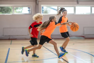 Foto op Plexiglas Kids in bright sportswear playing basketball together and feeling competitive © zinkevych