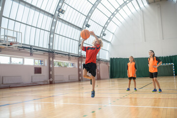 Blonde boy in red tshirt jumping with a ball in hands