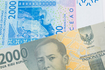 A macro image of a grey two thousand Indonesian rupiah bank note paired up with a blue, two thousand West African franc bank note.  Shot close up in macro.