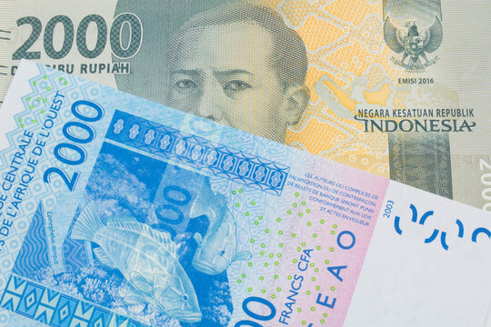 A macro image of a grey two thousand Indonesian rupiah bank note paired up with a blue, two thousand West African franc bank note.  Shot close up in macro.