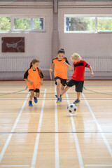 Three kids in sportswear playing indoors football in the gym