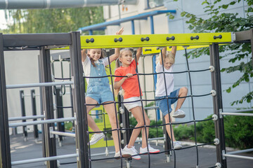 Three kids climbing on outdoor playground and looking excited