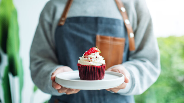 A waitress holding and serving a piece of red velvet cupcake