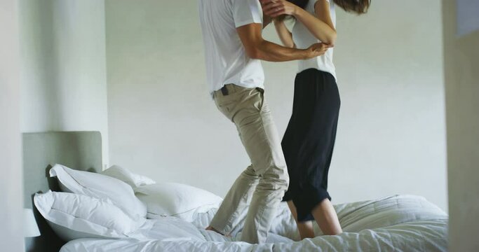 Young just married couple in love having fun and dancing while listening to the music on a bed in the bedroom in the morning.