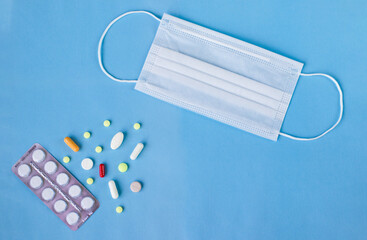 medical mask and multicolored pills on a blue background