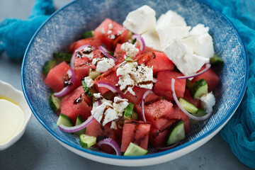 Close-up of salad with watermelon cubes, feta cheese, chopped cucumber, red onion and balsamic sauce served in a blue plate