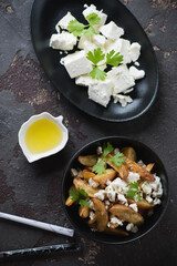 Bowl of baked potato wedges served with feta cheese in a greek style, flatlay on a brown stone background, vertical shot