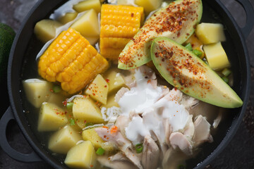 Ajiaco or colombian potato, chicken and corn stew topped with avocado and sour cream, close-up, high angle view