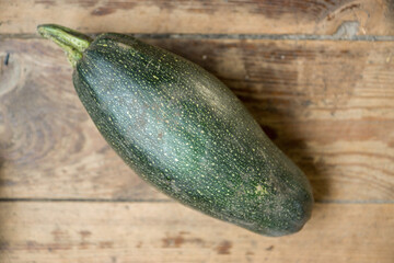 Top view of a ripe large zucchini plucked from the garden bed and lying on a wooden surface. Selective focus, shallow depth of field