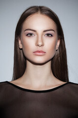 Beauty people portrait. Female model of a natural skin, wear in black dress, looking at camera, over grey background.