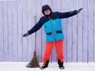 man in bright ski suit stands holding broom in his hands and is going to clean the snow in winter...