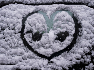 Snow covered car side window with drawn letters and hearts