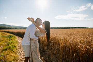 Naklejka na ściany i meble Young couple in the wheat field on sunny summer day. Couple in love have fun in golden field. Romantic couple in casual clothe outdoodrs on boundless field