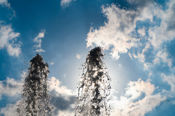 Shape of water, fountain water jet close up on blue sky and sun background.