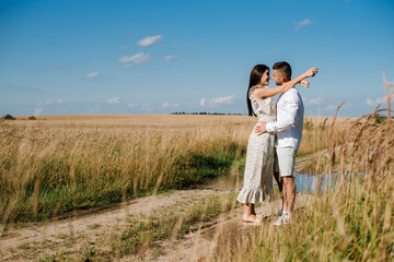 Young couple in the wheat field on sunny summer day. Couple in love have fun in golden field. Romantic couple in casual clothe outdoodrs on boundless field