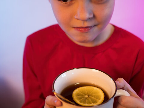 Funny Boy Blond Got Sick And Is At Home In Quarantine. Child Drinks Hot Tea From Large Bright Mug. In Cup Of Tea With Lemon And Honey. Baby Wants To Get Well Soon