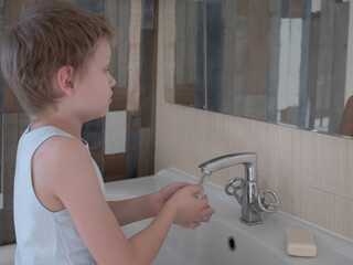 Happy boy washes hands with soap. Child playing with bar of soap and water in sunny bathroom with window. Water activities for children. Hygiene and skin care for children. Bathroom interior