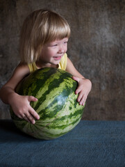 Fototapeta premium Funny blond boy hugs big watermelon lying on table with his hands