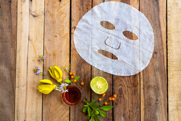natural aroma sheet mask extract honey, lemon herbal vegetation  health care for skin face essence face mask and flower ylang ylang arrangement flat lay style on background wooden