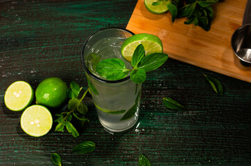 Mojito, cóctel de origen cubano, sobre mesa verde decorada con ingredientes del cóctel. Fondo de madera.