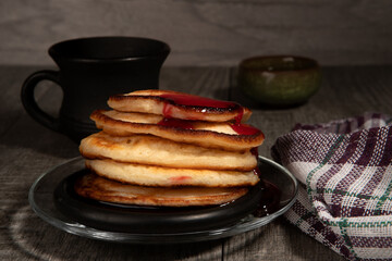 Several pancakes with cherry jam on wood background