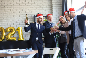 Business people are celebrating holiday in modern office drinking champagne and having fun in coworking. Merry Christmas and Happy New Year 2021.