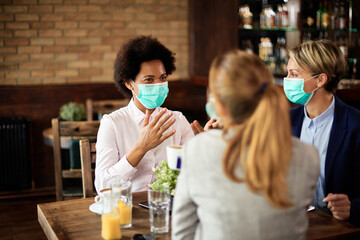 Happy businesswomen wearing protective face masks while talking in a cafe.