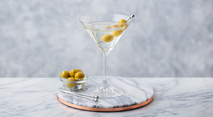 Martini cocktail with green olives on marble cutting board. Grey background. Close up.