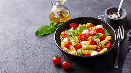 Pasta fusilli with mozzarella cheese, tomatoes and basil. Gray background. Copy space.