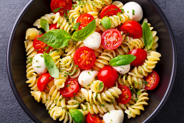 Pasta fusilli with mozzarella cheese, tomatoes and basil. Grey background. Close up.
