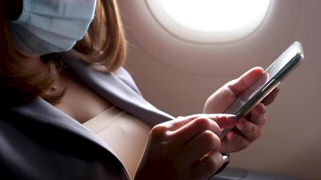 Close up hand of Young business woman Using smartphone on an Airplane.,woman wearing face mask on an airplane travel concept new normal background.during coronavirus or covid-19 virus outbreak