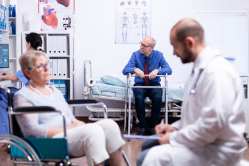 Senior man sitting on hospital bed with walking frame wainting for consultation. Man with disabilities ,walking frame sitting in hospital bed. Health care system, clinic patients.