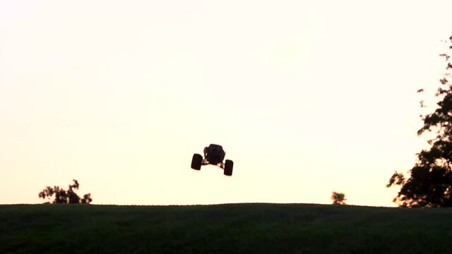 Monster rc car jumps high in slow motion. Flight of radio controlled car. Green field and evening sky.
