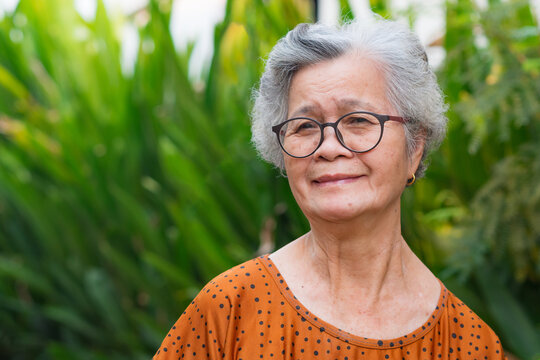 Portrait of a senior Asian woman wearing eyeglasses looking at camera while standing in a garden
