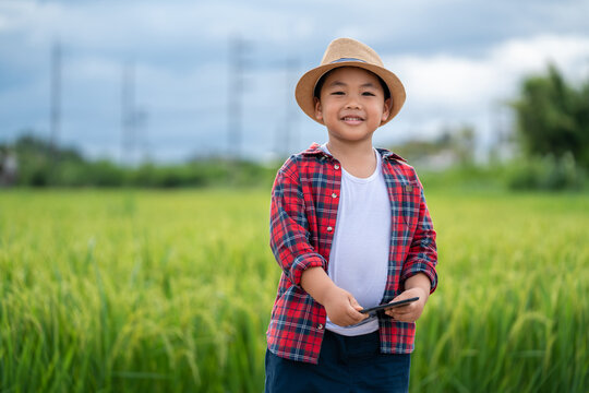 Asian Little boy with a tablet Looking at the camera interested in learning the surroundings in the green fields, education concept outside the classroom Educational freedom In the age of technology