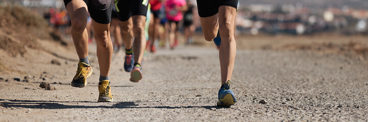 Runners running shoes on trail run. Ultra running athletes legs close up on running in rock path...