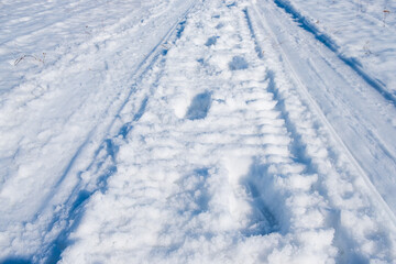 Fototapeta na wymiar footprints of a person in the snow against the background of snowmobile tracks