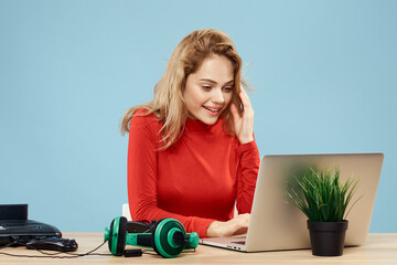 Fototapeta na wymiar Woman sitting at a table in front of a laptop headphones controller playing online lifestyle blue background